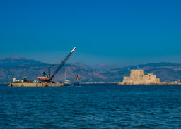The second huge crane claws mud and silt from the bottom.  The Bourtzi Island Fortrress watches silently.